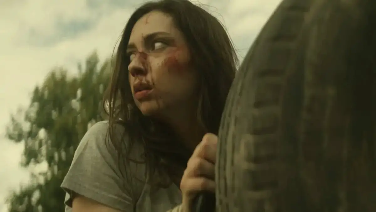 Girl with Injuries crouches near a tire looking back