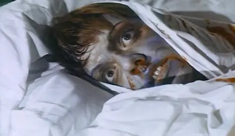 Gray, horrified face peers from under covers in a bed