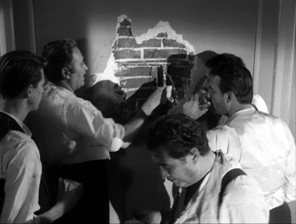 Guys peel back wallpaper to find brick wall in The Extermination Angel