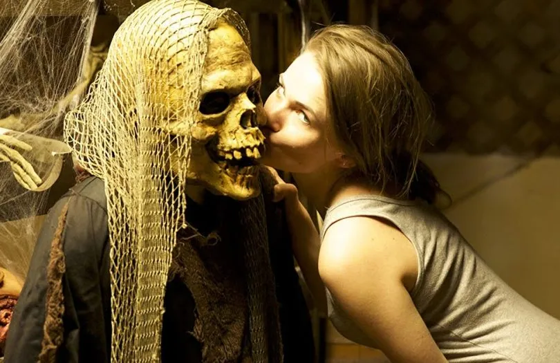 Girl kisses figure in skull mask