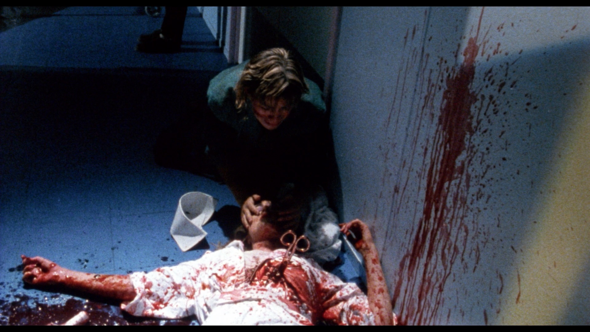 Guy leans over bloody body that's stabbed with scisors
