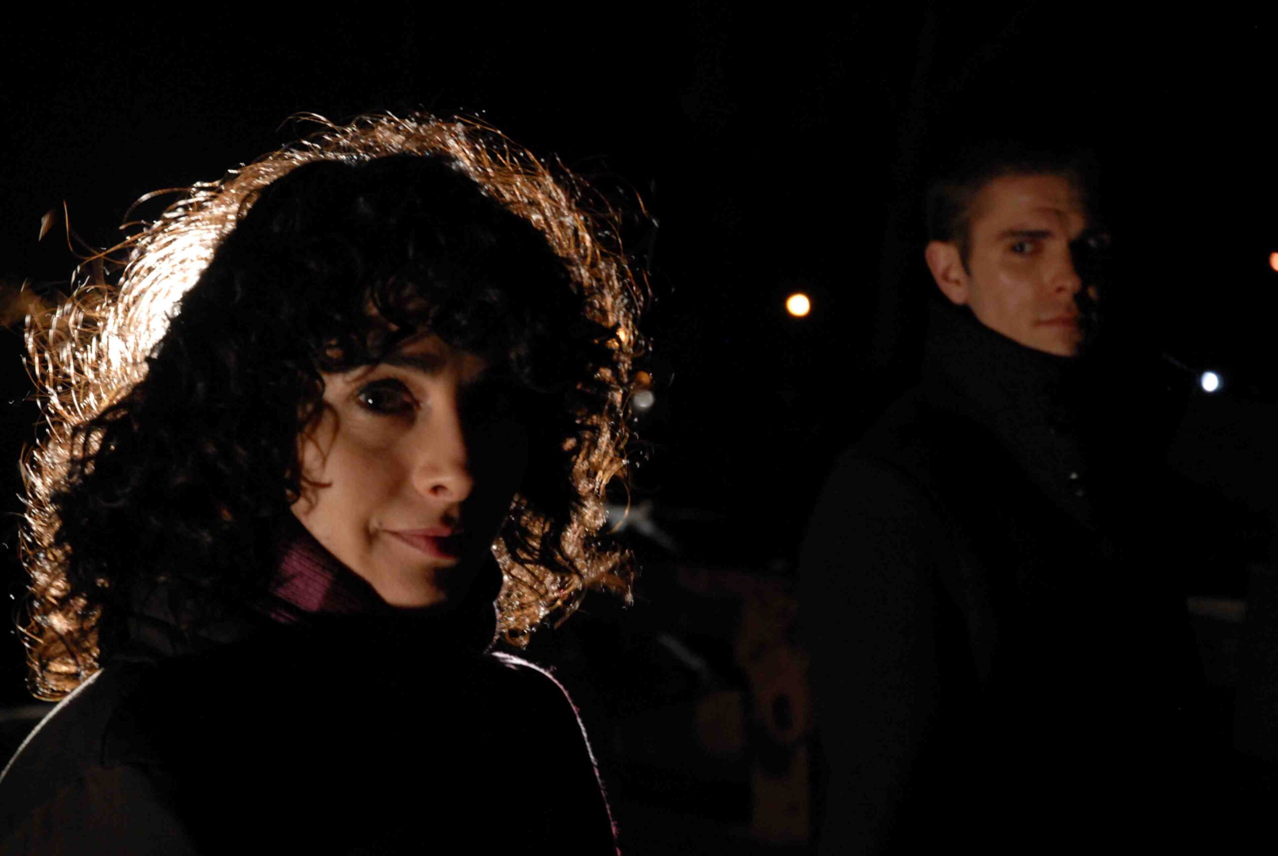 In shadowing spot woman looks toward camera as man looks on at her