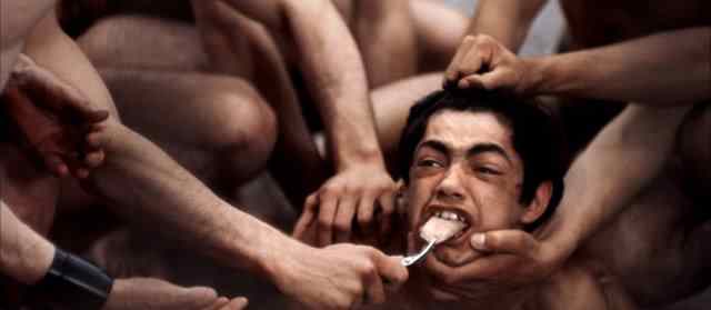 Torture seen in where this young man gets his tongue cut off as the leaders watch from within the building.